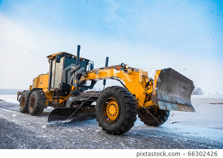 Motor Graders, Grader Road Construction. Industrial machine on construction of roads. Truck moving on dirt country road. Grader is driving along an empty winter road 66302426