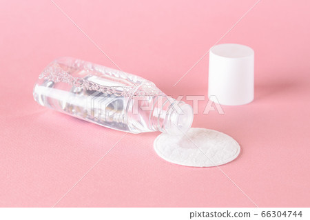 Skin tonic lotion or micellar water dripping from open bottle onto a cotton pad on a pastel pink. 66304744