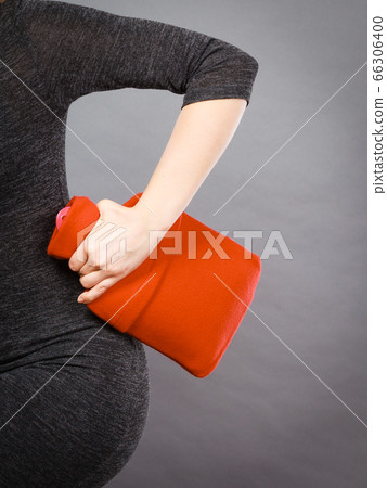 Woman holds hot water bottle in red fleece cover Woman holds hot water bottle in red fleece cover 66306400