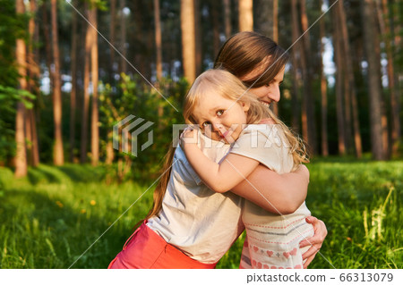 Toddler daughter hugs her mom outdoors Toddler daughter hugs her mom outdoors 66313079