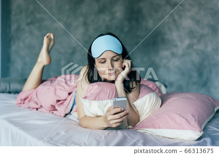 .the girl in bed woke up and looks at the phone .the girl in bed woke up and looks at the phone 66313675