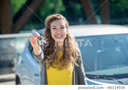 Smiling woman with car key in outstretched hand 66314936