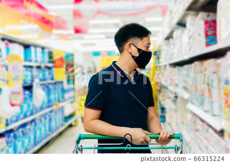 Young adult Asian man wearing a face mask while shopping with cart trolley in grocery supermarket store. 66315224