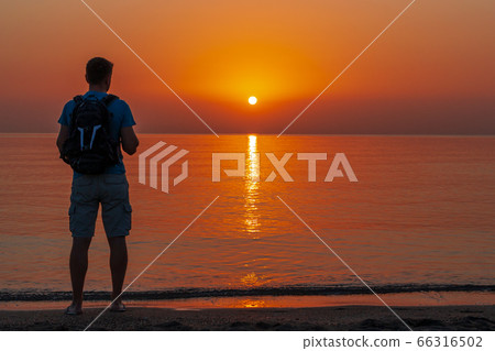 A man with a backpack stands on the beach and 66316502