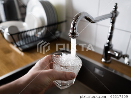 male's hand pouring water into the glass from chrome faucet to drink running water with air bubbles. potable water and safe to drink. man filling a glass of water from a stainless steel kitchen tap 66317309