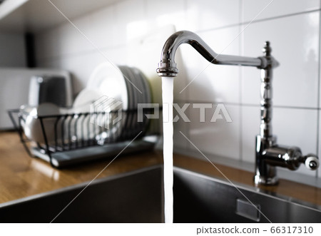 Water flowing out of a kitchen stainless steel tap into the sink. Wasting water by leaving a chrome faucet tap running. Water misuse in domestic duties and activities. Overusing household water. 66317310