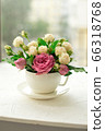 A bouquet of white roses in a cup on a white table opposite the window 66318768