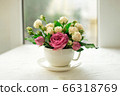 A bouquet of white roses in a cup on a white table opposite the window 66318769