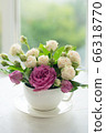 A bouquet of white roses in a cup on a white table opposite the window 66318770