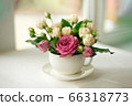 A bouquet of white roses in a cup on a white table opposite the window 66318773