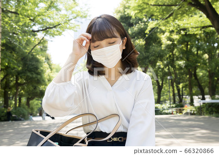 A young woman wearing a mask and sitting on a park bench 66320866