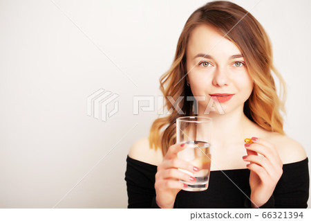 Young woman holding a glass of water and a pill for weight loss 66321394