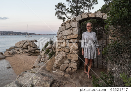 Beautiful woman in luxury summer dress enjoying peaceful seascape of Porto Rafael bay at Mediterranean sea of Costa Smeralda, Sardinia, Italy at dusk Beautiful woman in luxury summer dress enjoying peaceful seascape of Porto Rafael bay at Mediterranean sea of Costa Smeralda, Sardinia, Italy at dusk 66321747
