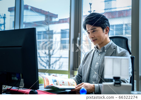 A middle-aged man operating a computer while looking at materials (business casual) A middle-aged man operating a computer while looking at materials (business casual) 66322274