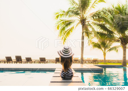 asian woman relax around outdoor swimming pool in hotel resort with palm tree at sunset or sunrise asian woman relax around outdoor swimming pool in hotel resort with palm tree at sunset or sunrise 66329007