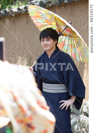 A man wearing a kimono and holding a Japanese umbrella 66329575