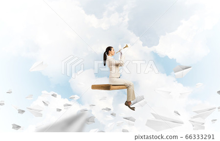 Young woman playing trumpet and sitting on book Young woman playing trumpet and sitting on book 66333291