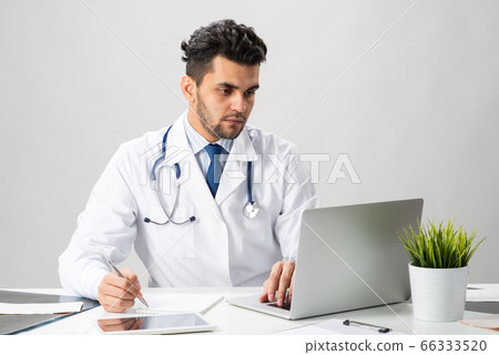 Handsome doctor sitting at desk in office Handsome doctor sitting at desk in office 66333520