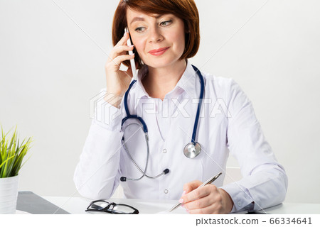 Attractive redhead doctor talking on smartphone Attractive redhead doctor talking on smartphone 66334641