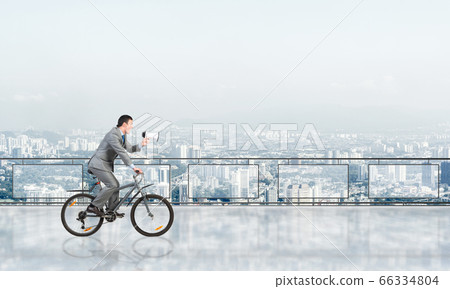 Businessman with megaphone in hand on bike 66334804