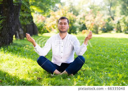Young man meditates in lotus pose on green grass Young man meditates in lotus pose on green grass 66335048