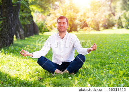 Young man meditates in lotus pose on green grass 66335533