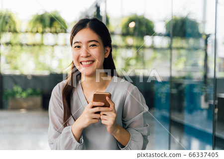 Young 20s Asian beautiful girl holding a mobile phone in window glass building scene. 66337405