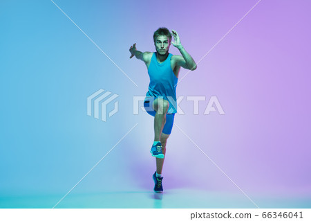 Full length portrait of active young caucasian running, jogging man on gradient studio background in neon light 66346041