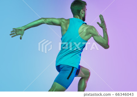 Full length portrait of active young caucasian running, jogging man on gradient studio background in neon light 66346043