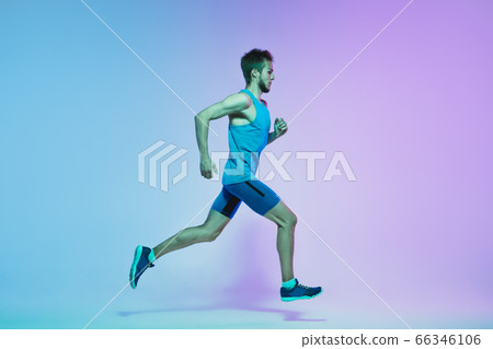 Full length portrait of active young caucasian running, jogging man on gradient studio background in neon light 66346106