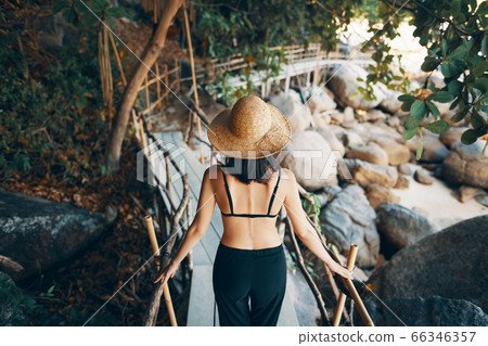 Back view of young woman in straw hat walking on wooden bridge in tropical island Back view of young woman in straw hat walking on wooden bridge in tropical island 66346357