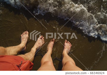 Top view on naked feets on sand in foaming sea wave. 66346924