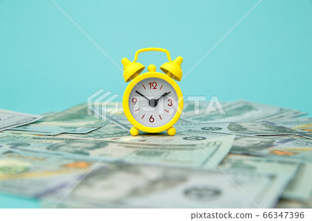 Close-up of yellow alarm clock and money on blue background. Business Finance and Money concept. Save money for prepare in the future. Time is money concept Close-up of yellow alarm clock and money on blue background. Business Finance and Money concept. Save money for prepare in the future. Time is money concept 66347396
