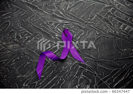 A purple ribbon for the awareness about the unacceptability of the violence against women on a dark gray surface 66347447