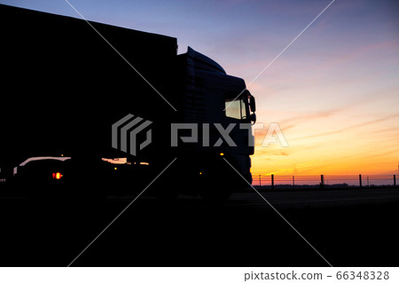 A truck with a trailer rides on the motorway at night against the backdrop of an orange sunny sunset. The concept of the regime of work and rest of truckers, copy space, tachograph A truck with a trailer rides on the motorway at night against the backdrop of an orange sunny sunset. The concept of the regime of work and rest of truckers, copy space, tachograph 66348328