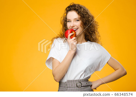 Pretty girl with curly hair holding fresh apple Pretty girl with curly hair holding fresh apple 66348574