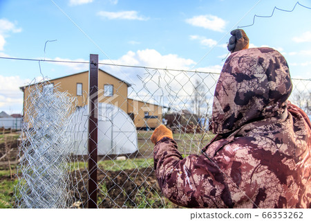 A man sets a metal mesh on the fence. 66353262