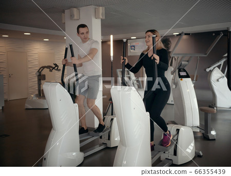 Modern gym - a guy in white t-shirt and a woman doing morning exercises in the gym 66355439