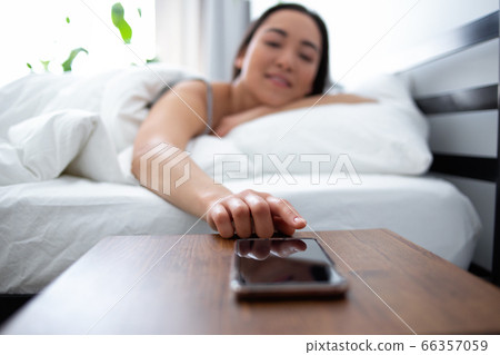 Smiling woman touching smartphone after waking up 66357059