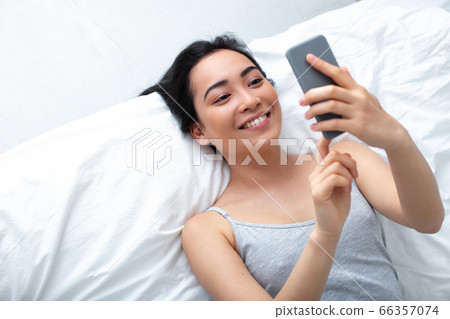 Cheerful young woman using cell phone for pleasure indoors 66357074