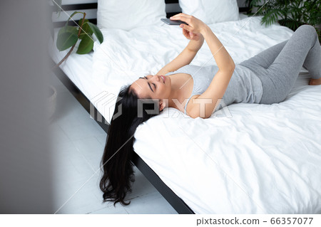 Jolly young woman with smartphone on bed 66357077