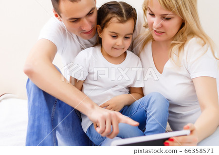 An attractive happy, family of mother, father and daughter sitting on a sofa at home having fun using a tablet computer 66358571