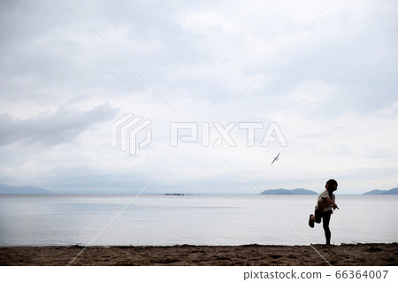 Silhouette of a boy flying a toy plane on the sandy beach 66364007