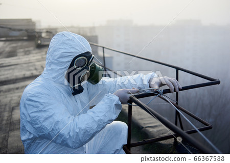 Worker scientist wearing protective coverall and gas mask doing ecological tests on the roof 66367588