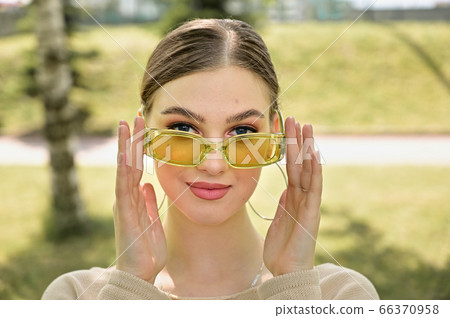 Close-up portrait of a cute caucasian young woman with excellent make-up. A model looks straight over glasses in a city park in sunny summer weather 66370958