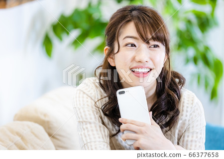 一個女人微笑著看著在客廳裡的沙發上的智能手機 一個女人微笑著看著在客廳裡的沙發上的智能手機 66377658