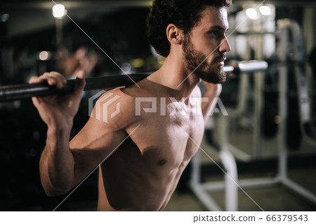 Middle shot portrait of Sportive bearded man with muscular body doing squats using heavy barbell Middle shot portrait of Sportive bearded man with muscular body doing squats using heavy barbell 66379543