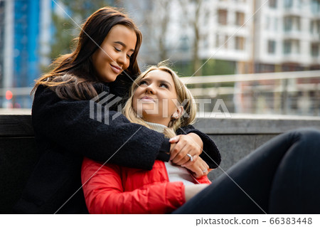 Smiling Best Friends Embracing And Sitting On The Ground In City Smiling Best Friends Embracing And Sitting On The Ground In City 66383448