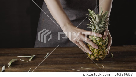 Woman' hands with ripe juicy natural organic tropical fruit pineapple on a wooden kitchen table on a black background. Woman' hands with ripe juicy natural organic tropical fruit pineapple on a wooden kitchen table on a black background. 66386698
