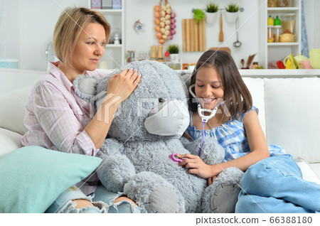 Girl and mother playing with toy bear in facial mask. Girl with stethoscope Girl and mother playing with toy bear in facial mask. Girl with stethoscope 66388180